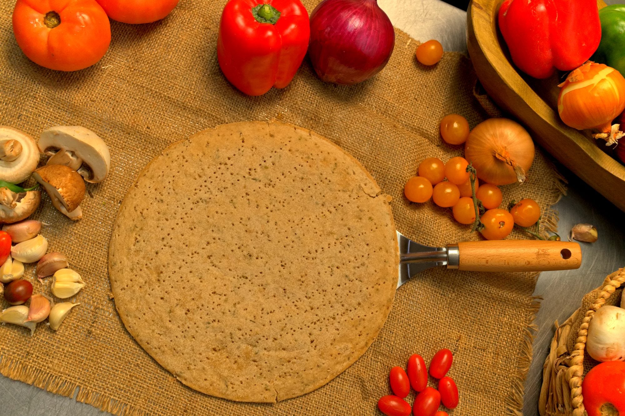 Base de pizza de pana sobre tela de saco, rodeada de vegetales