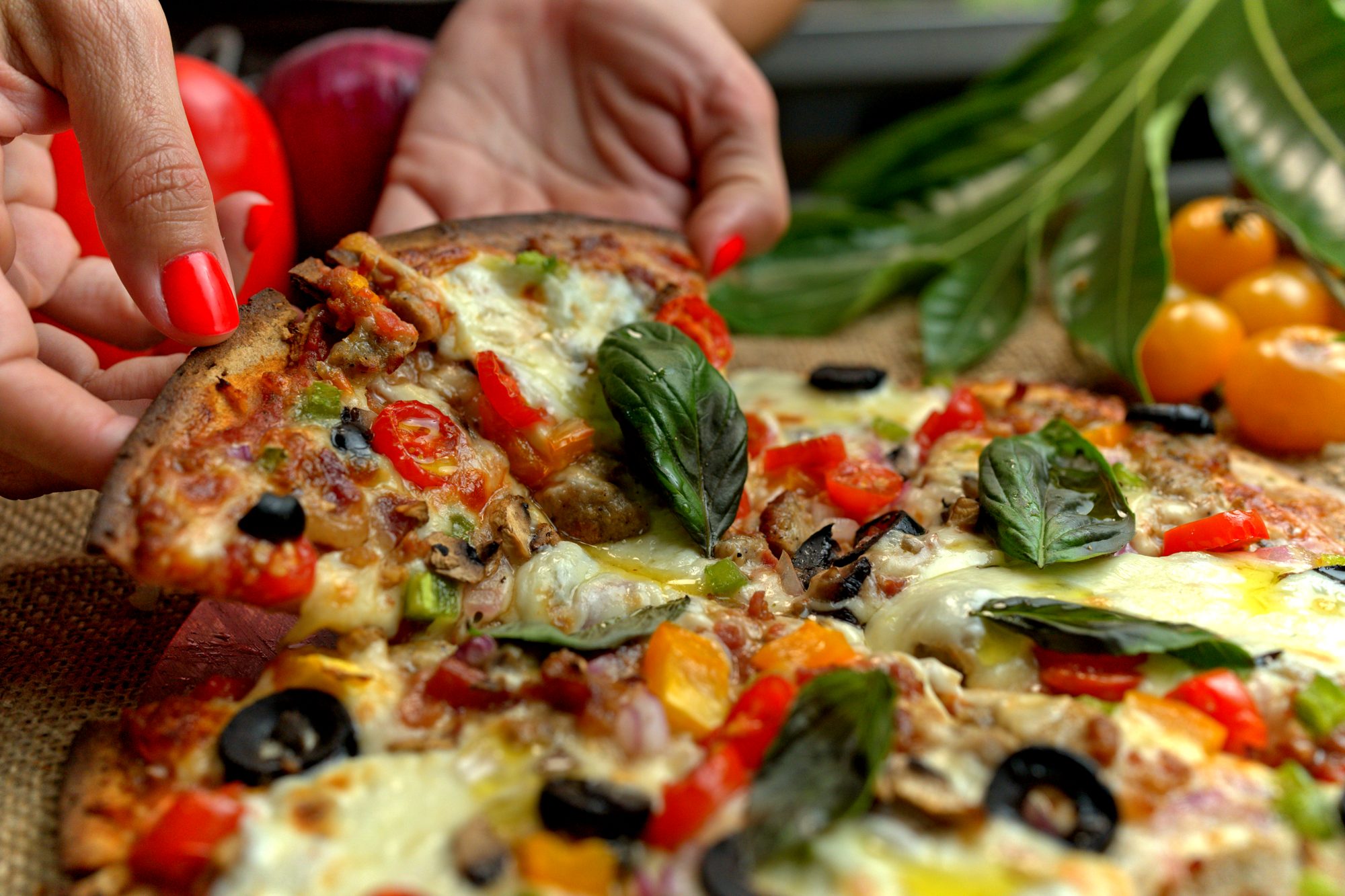 Manos tomando un slice de pizza de pana con vegetales y albahaca